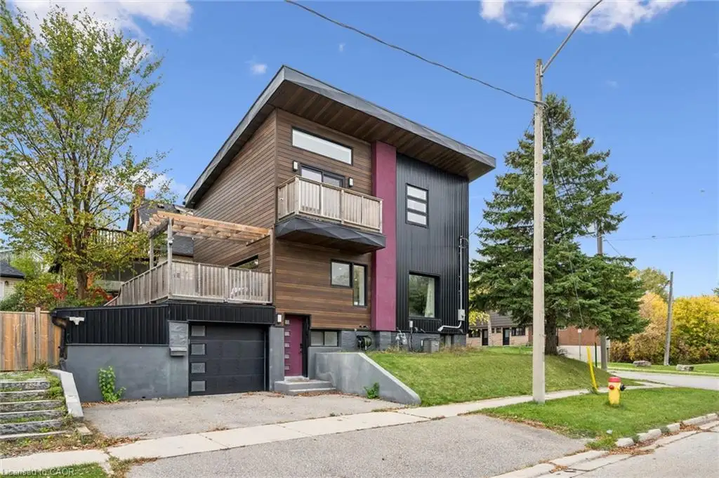 Modern multi-level exterior featuring wood-finish siding, black metal paneling, a private balcony, an attached garage, and a timber-frame pergola