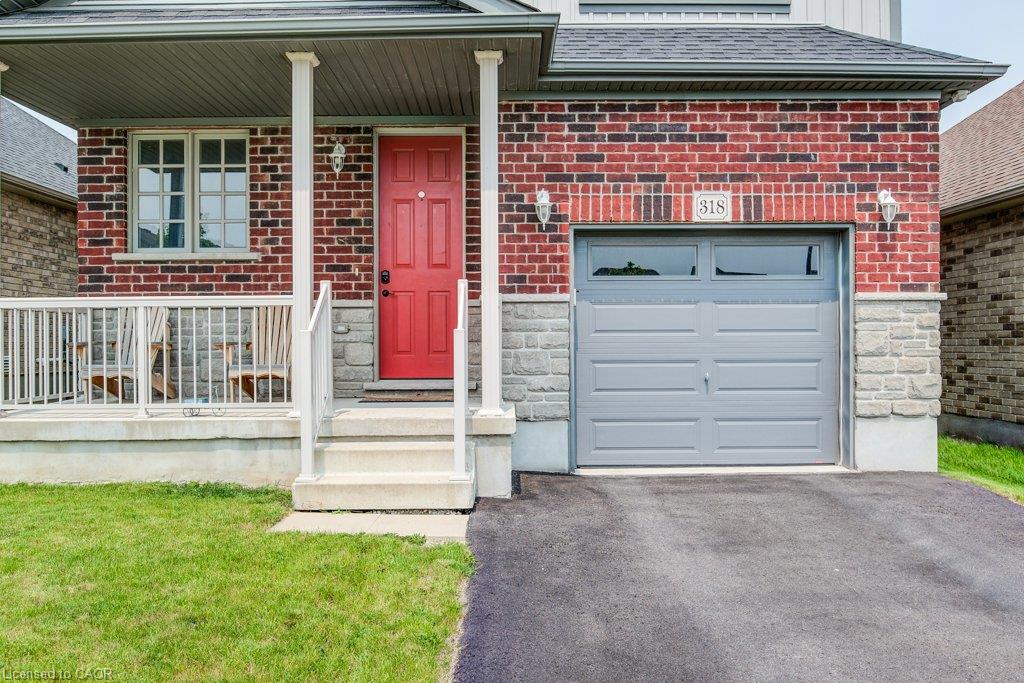 Brick exterior with stone accents, a covered porch with white railings, a red entry door, and an attached single-car garage with a paved driveway
