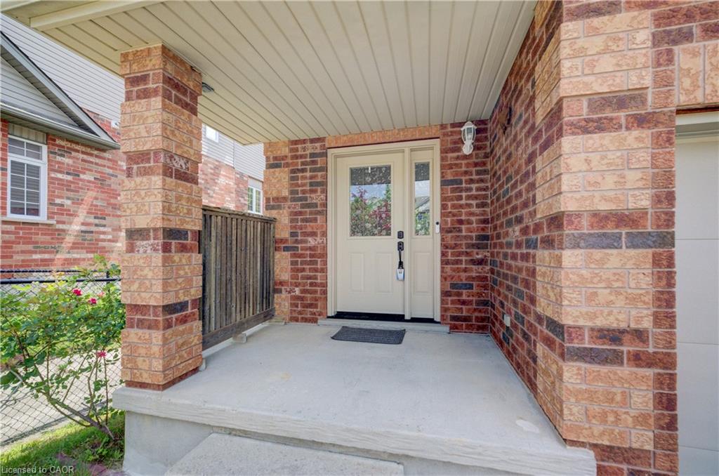 Inviting front porch featuring a multi-toned brick facade, covered entry, light-colored entry door with glass inserts, and a built-in wall sconce