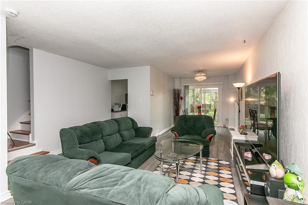 Open living area showcasing multiple seating zones with green upholstered furnishings, geometric patterned flooring, recessed ceiling lighting, and abundant natural light from expansive glass doors and windows opening to outdoor spaces