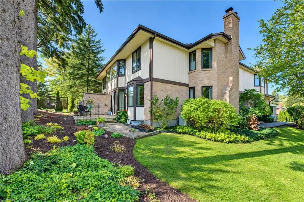 Multi-level exterior featuring a brick and vertical siding facade, masonry chimney, bay windows, and stone-paved patio set within a landscaped yard