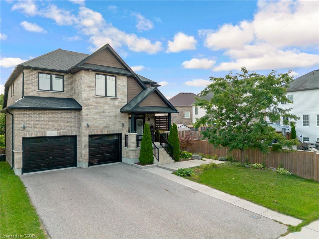 Stone and brick exterior with dark trim accents, double garage with dark doors, front porch with black railing, paved driveway, and established front yard landscaping