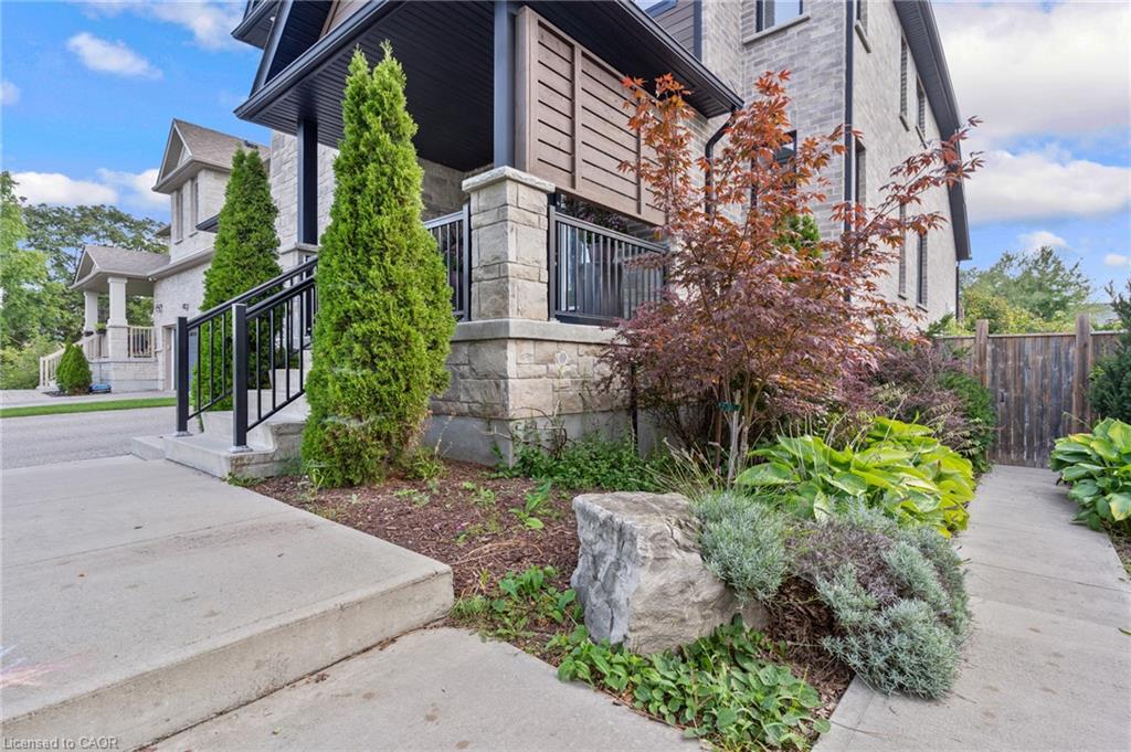 Stone facade, front porch with black railing, mature landscaping, concrete walkways, and wood fencing