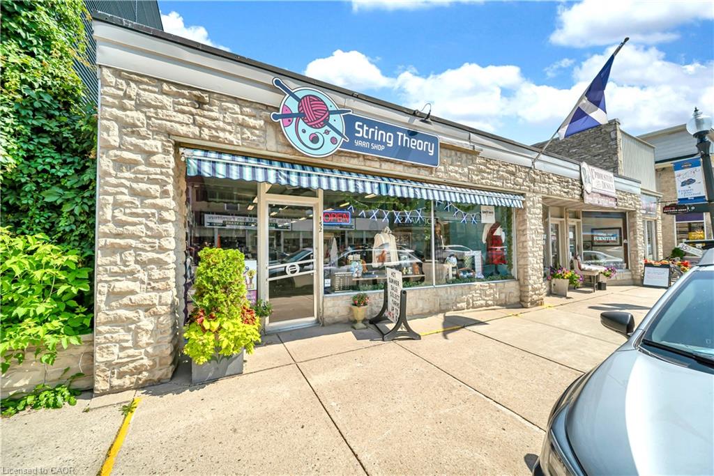 Street-facing storefront featuring a stone facade with integrated ivy-covered wall, striped awning, and recessed entrance with glass doors and sidelights