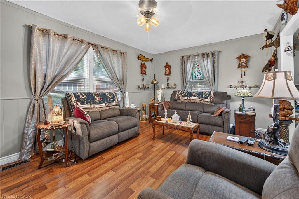 Living area featuring wood-finish flooring, light gray walls with wainscoting, and large windows with blinds