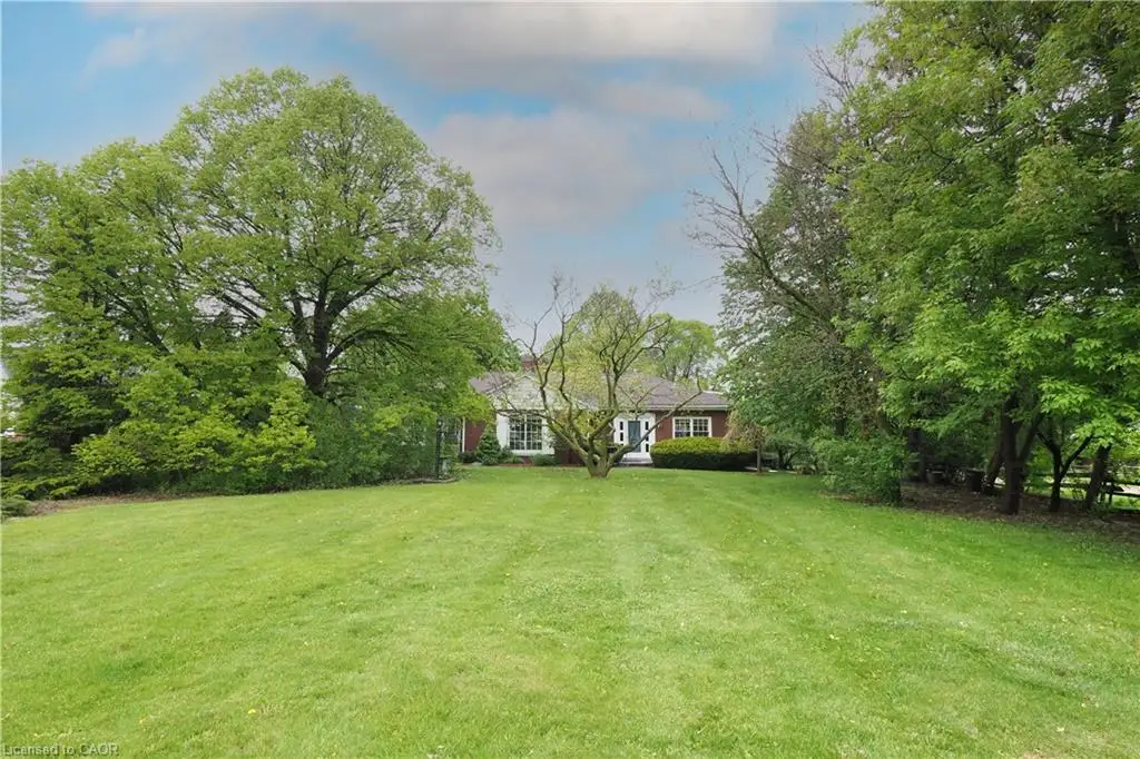 Expansive green lawn with mature trees and a brick-sided residence featuring white trim and multiple windows