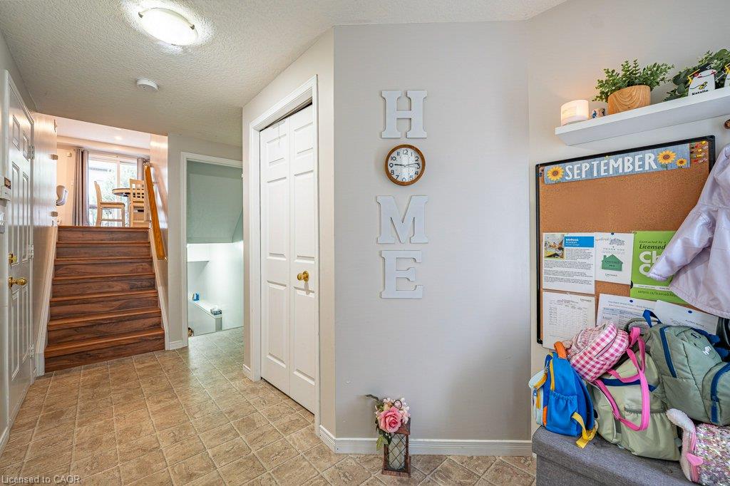Tiled flooring with a warm-toned wood-finish staircase and handrail, featuring white paneled doors and an overhead flush-mount light fixture