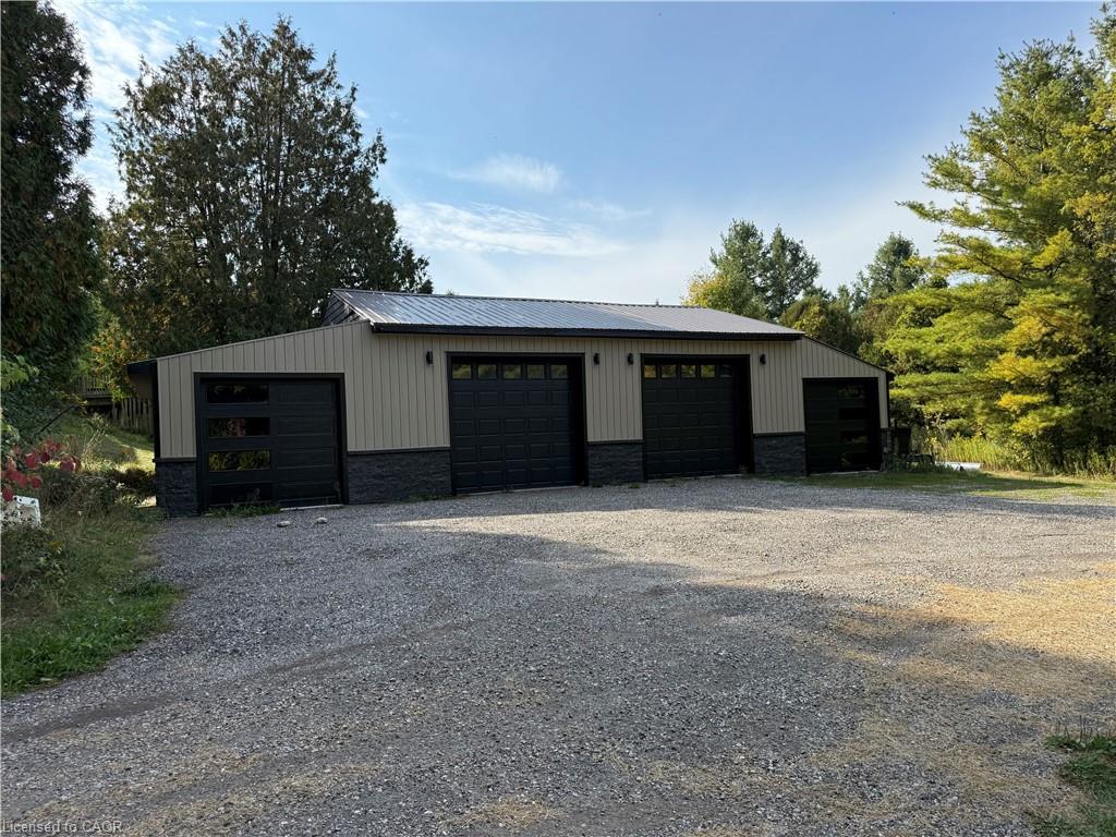 Metal-sided outbuilding featuring a metal roof, four garage bays, and a gravel surface