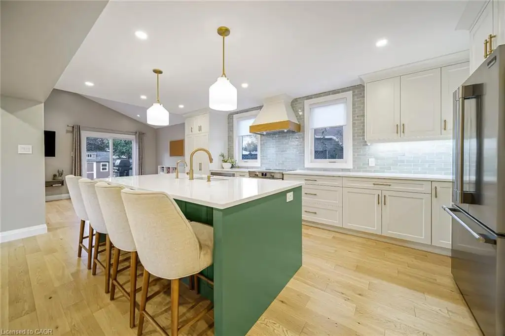 Spacious kitchen featuring a green island with a white countertop, stainless steel appliances, light wood-finish flooring, white cabinetry, and a subway tile backsplash