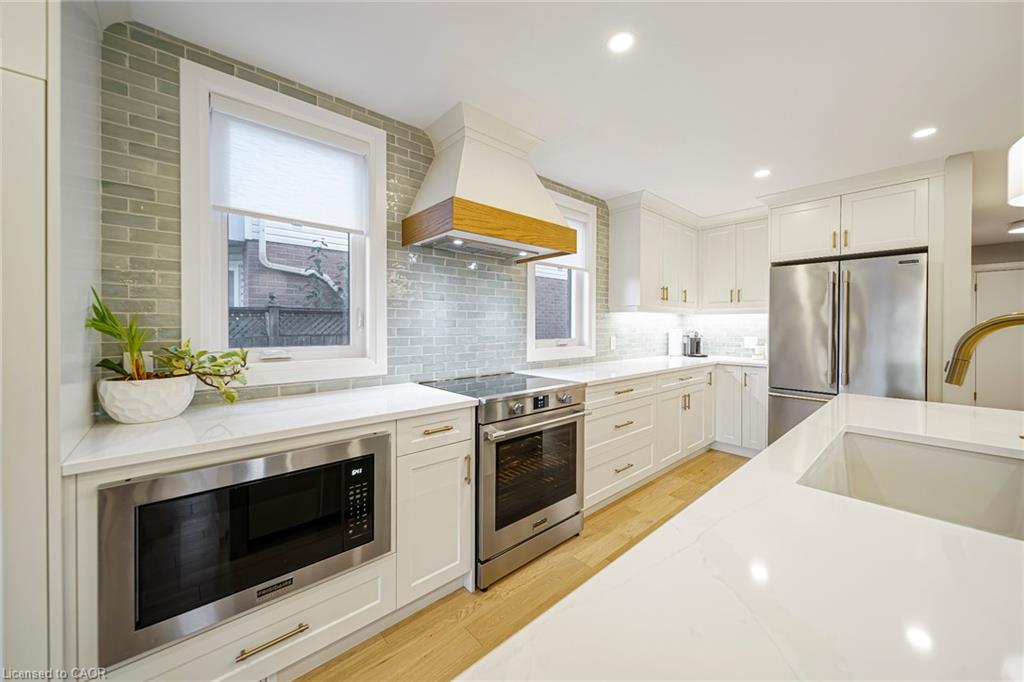 White cabinetry with gold-tone hardware, stainless steel appliances, light-toned wood-finish flooring, white countertops, and a subway tile backsplash