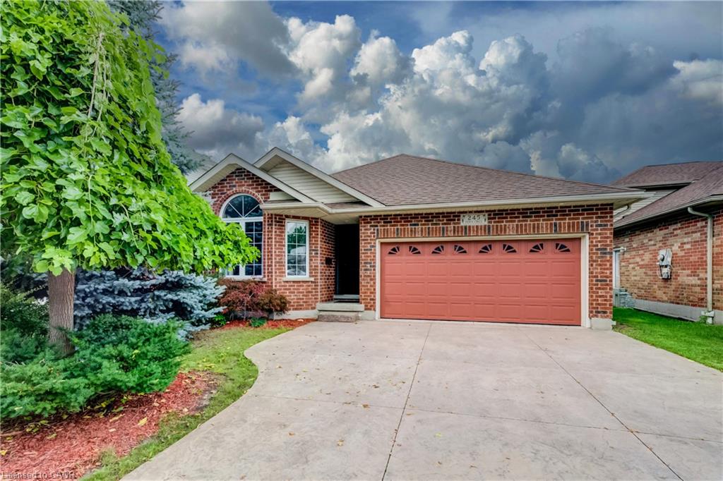 Brick exterior with an integrated garage, arched window, paved driveway, and mature landscaping