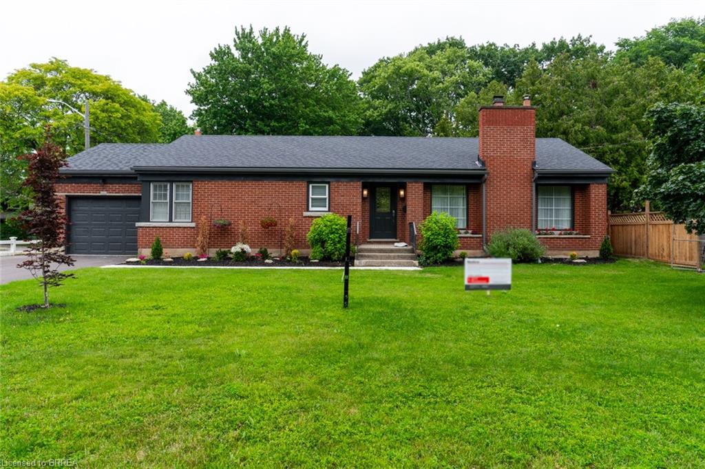 Brick bungalow with a dark gray shingled roof, a prominent brick chimney, and a landscaped front garden