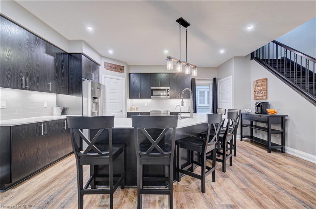 Modern kitchen with wood-finish flooring, dark wood-grain cabinetry, stainless steel appliances, and a central island with countertop seating