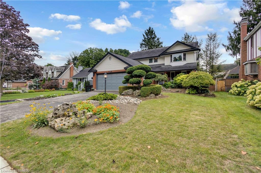 Exterior featuring a two-car garage, established landscaping, mature trees, and a paved driveway