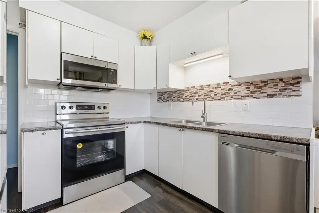 Kitchen with white cabinetry, stainless steel appliances, dual basin sink, and wood-finish flooring