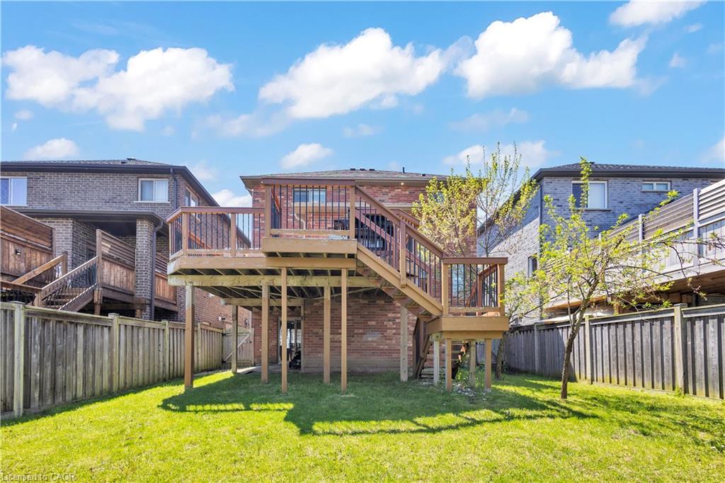 Elevated wood deck with baluster railings and staircase, brick exterior, and a spacious green lawn