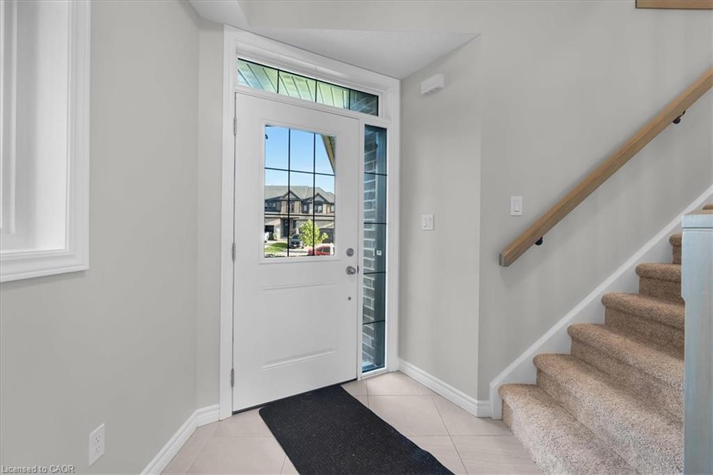 Entryway featuring a white door with window panes, a transom window, a side window, tiled flooring, and a carpeted staircase with a wood handrail