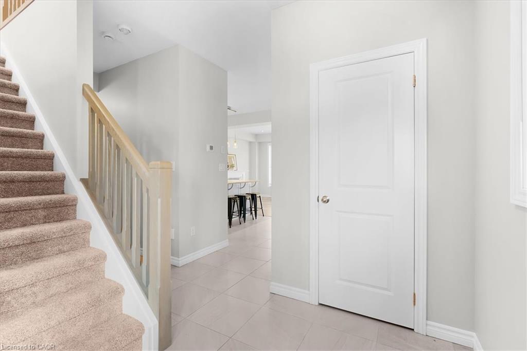 Tiled flooring, paneled interior door, carpeted staircase, light wood-finish handrail, and subtle wall sconce