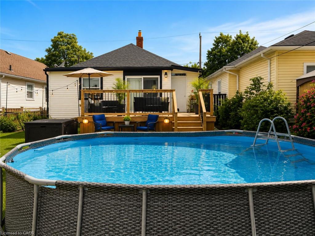 Backyard featuring an above-ground pool, a wooden deck with dark railings, a sliding glass door, and exterior wall lighting