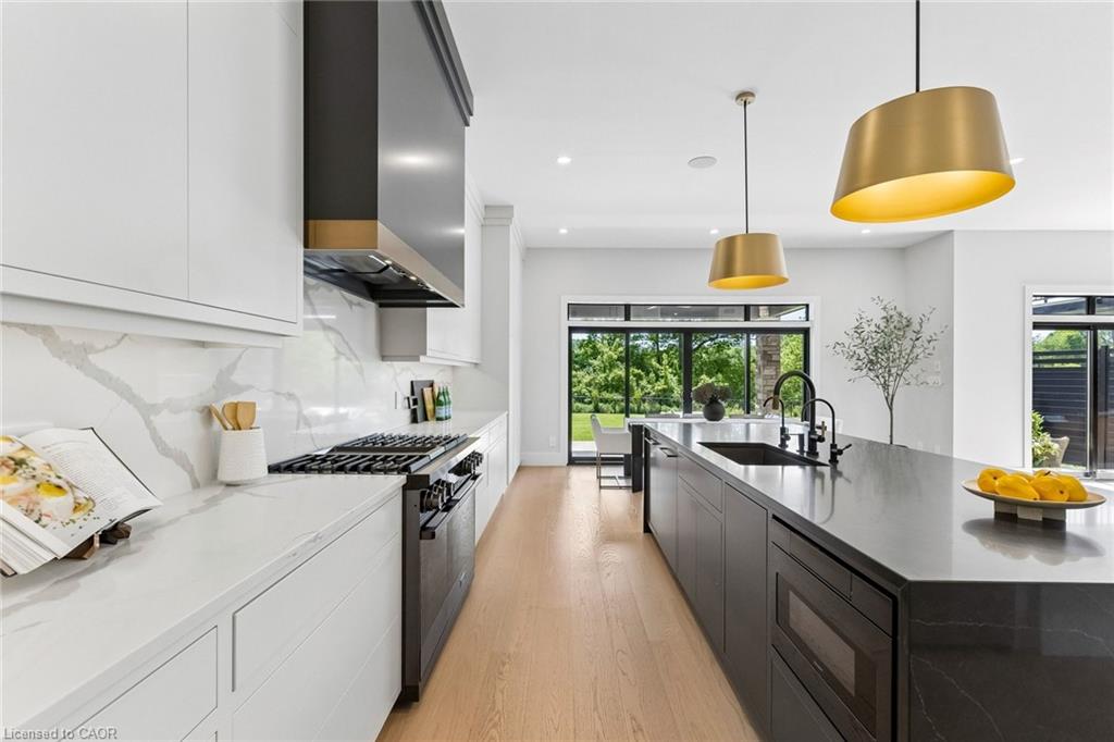 Gourmet kitchen featuring a built-in gas range, a dark range hood, light wood-finish flooring, white upper cabinetry, and a dark stone-finish island with integrated sink