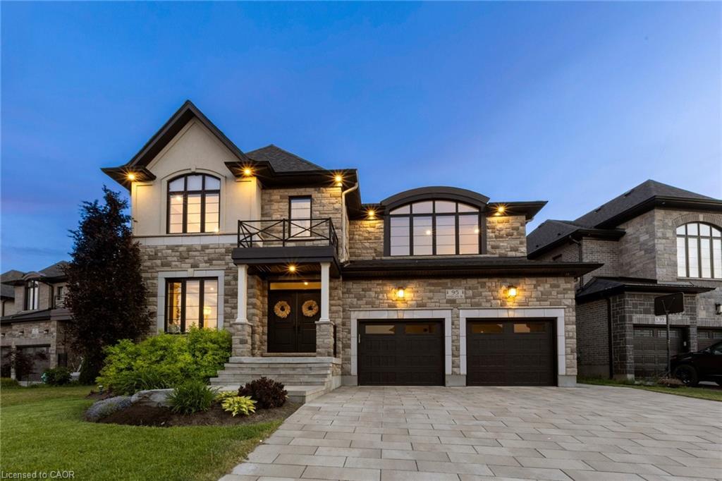 Stone and brick exterior with architectural lighting, arched windows, an over-sized two-car garage, a paver driveway, and a second-storey balcony