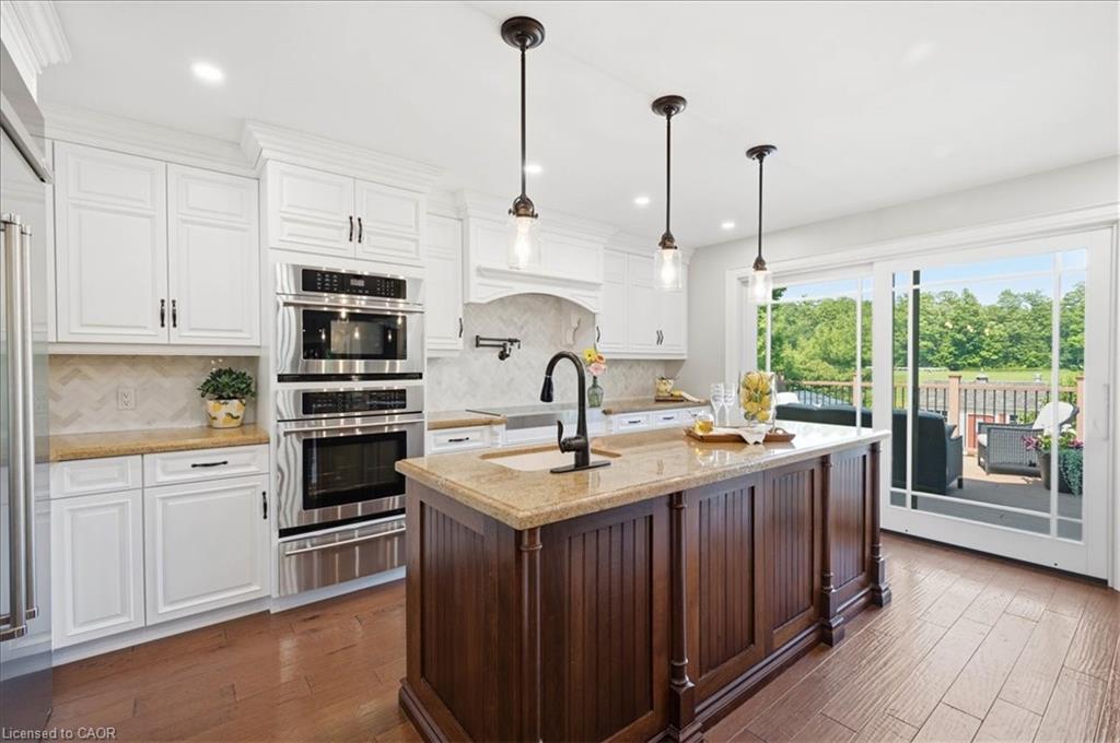Gourmet kitchen featuring a granite countertops, full suite of stainless steel appliances, white cabinetry, hand scraped engineered hardwood, and sliding glass doors opening to an exterior composite deck
