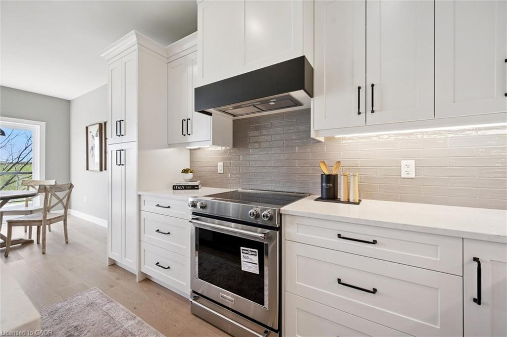 White shaker-style cabinetry with matte black hardware, stainless steel range, light-toned subway tile backsplash, under-cabinet lighting, and light wood-finish flooring