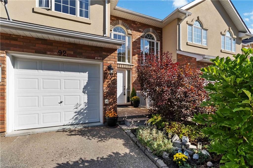 Welcoming front elevation showcasing a two-story brick and stone exterior with white-trimmed windows, white panel garage door, and a professionally landscaped entry featuring mature climbing ivy, seasonal plantings, and defined hardscaped beds