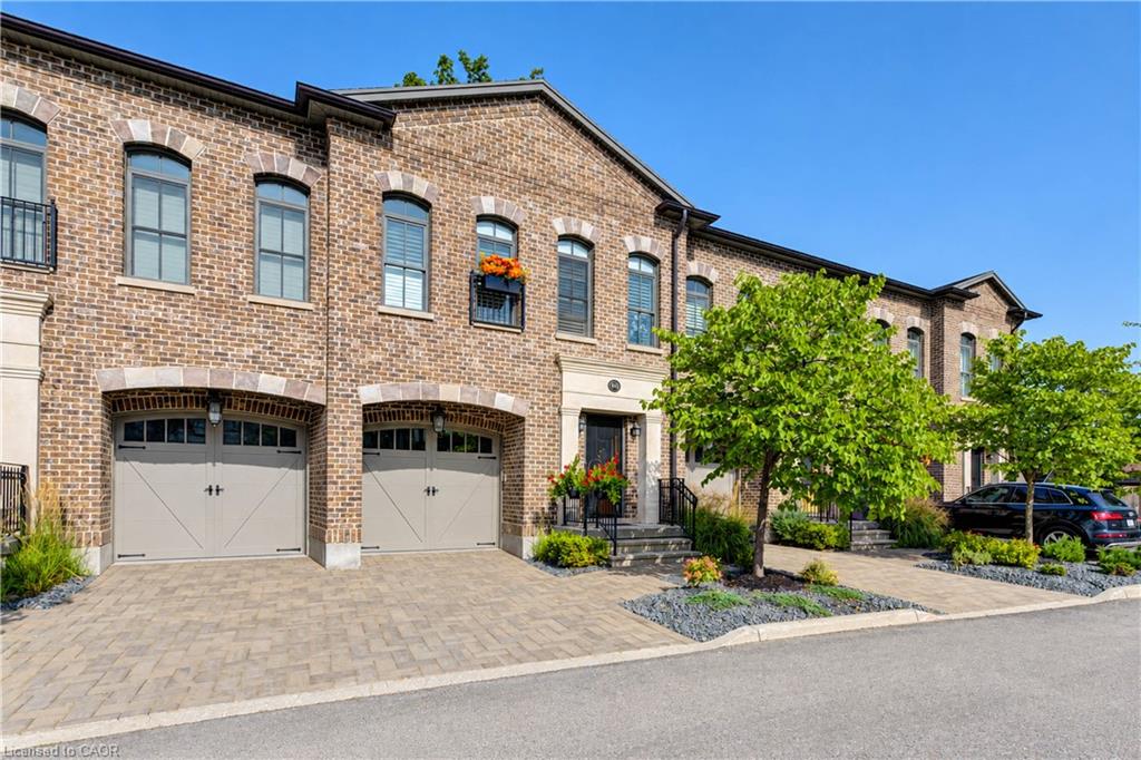 Brick exterior with arched window details, paver driveway, arched garage doors, decorative wrought iron balcony, and mature landscaping