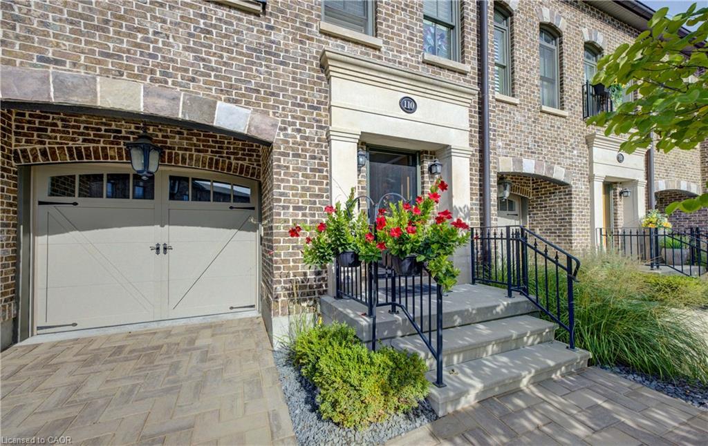 Brick exterior with stone accents, paver driveway, arched garage door, concrete entry stairs with wrought iron railings, and built-in entry lighting