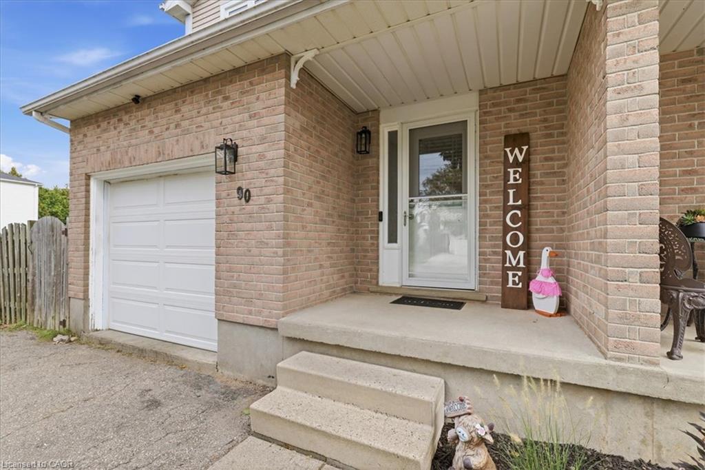 Brick exterior, attached garage, covered porch, concrete steps, and exterior lighting fixture