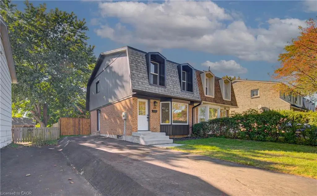 Gambrel roofline with dormer windows, brick lower facade, and mature landscaping