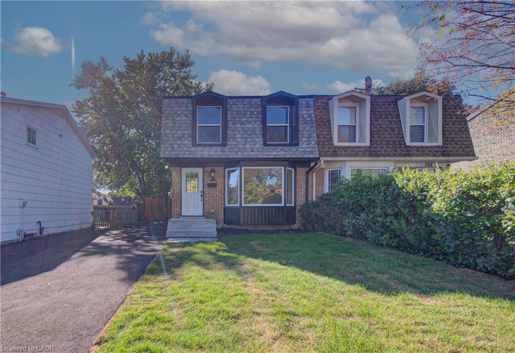 Brick exterior featuring a mansard roof, front lawn, and paved driveway