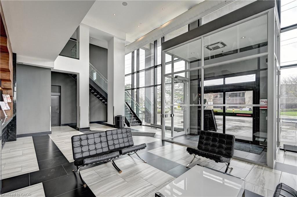 Lobby featuring a striking black and white geometric tile floor, double-height ceilings, a prominent glass-enclosed entry, full-height windows, and a multi-level staircase with glass railings