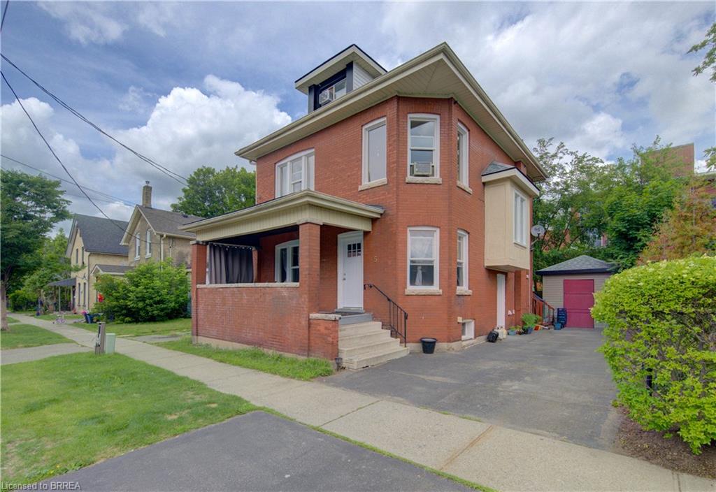 Brick exterior with multiple window styles, covered porch, dormer window, and an attached, paved driveway
