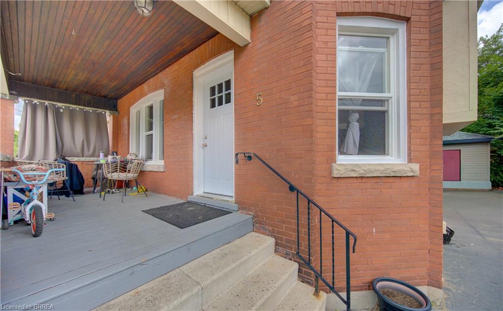 Brick facade residence featuring a covered porch with a wood-finish ceiling, concrete entry steps, a black metal handrail, and white-framed windows with stone sills