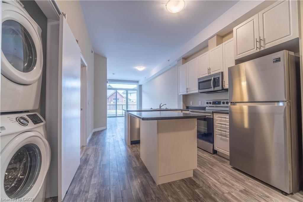 Kitchen with stainless steel appliances, white cabinetry, dark wood finished floors, a center island, and dark countertops