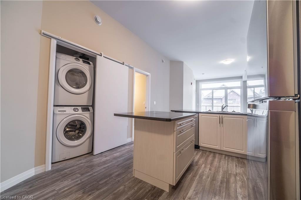 Kitchen with freestanding refrigerator, dark wood-type flooring, a center island, stacked washer and dryer, and a peninsula