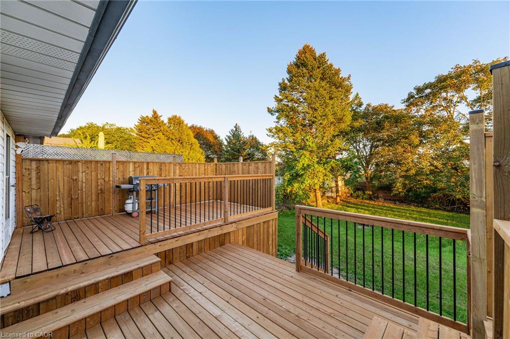 Two-tier wood deck with railings and steps, featuring a privacy fence and mature trees
