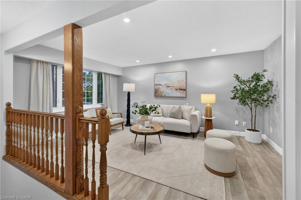 Recessed ceiling lighting, light gray wall paint, wood-finish flooring, white window trim, and a wood banister