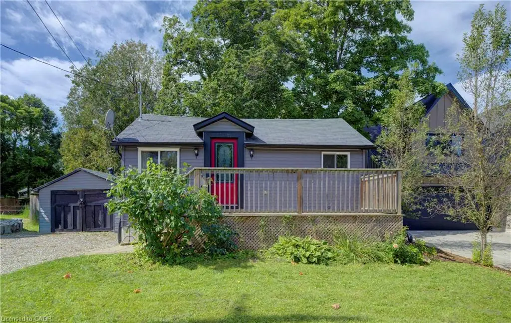 Gray exterior siding with a red entrance door, front wooden deck, and a detached garage with dark barn-style doors