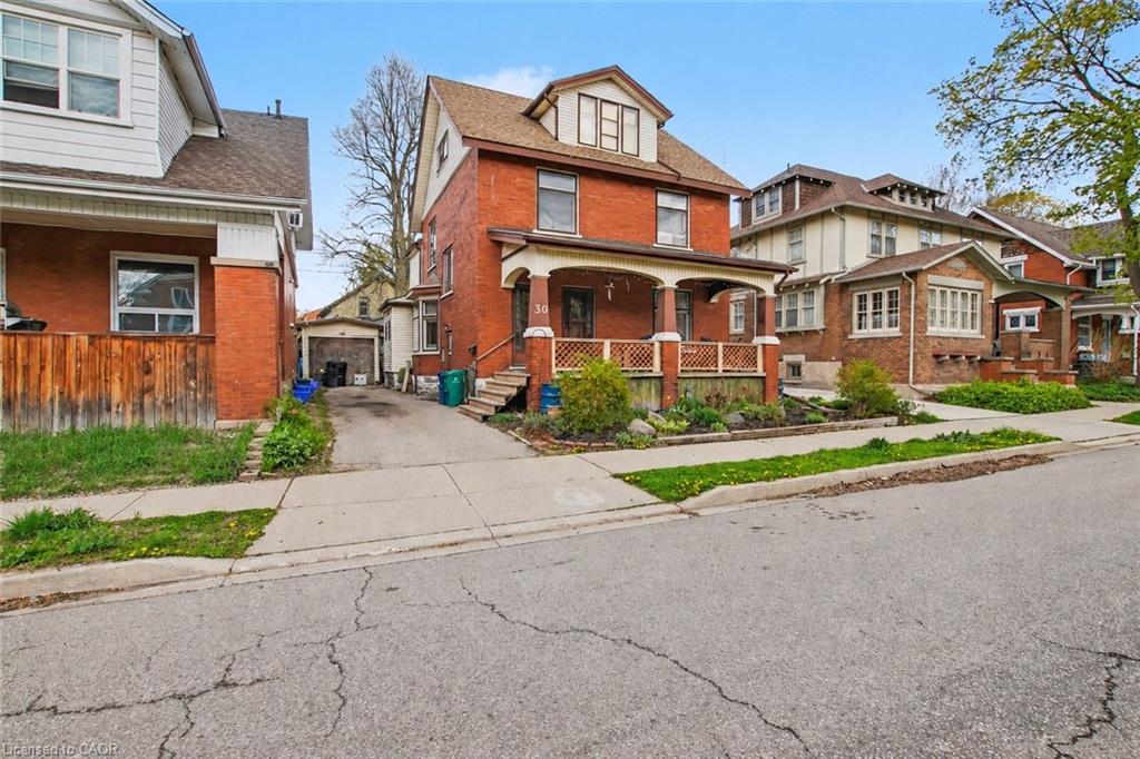 Brick exterior with a covered front porch featuring decorative railing, a paved driveway, and mature landscaping