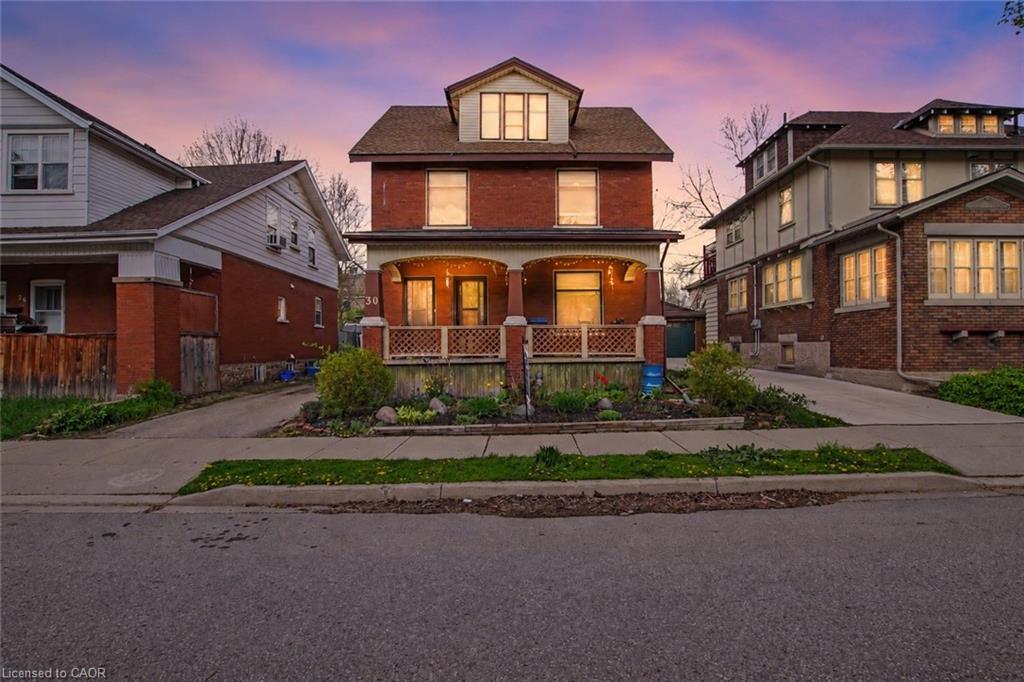 Brick-clad residence featuring a covered front porch with decorative railing, multiple window dormers, and a gabled roofline