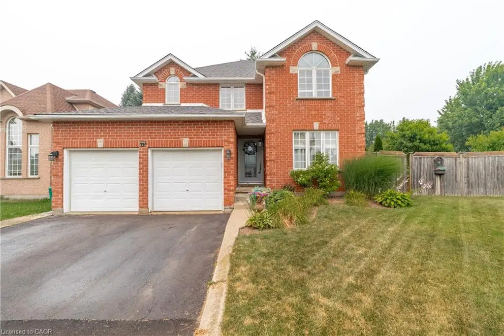 Brick exterior featuring a two-car garage, asphalt driveway, front entry with transom window, landscaped garden beds, and a grasse dfront yard