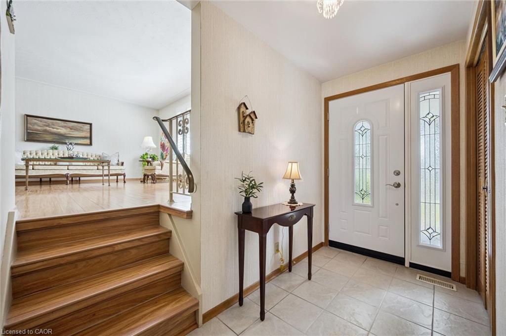 Entryway with white panel door featuring decorative glass inserts, ceramic tile flooring, and wood-finish stairs with a metal handrail
