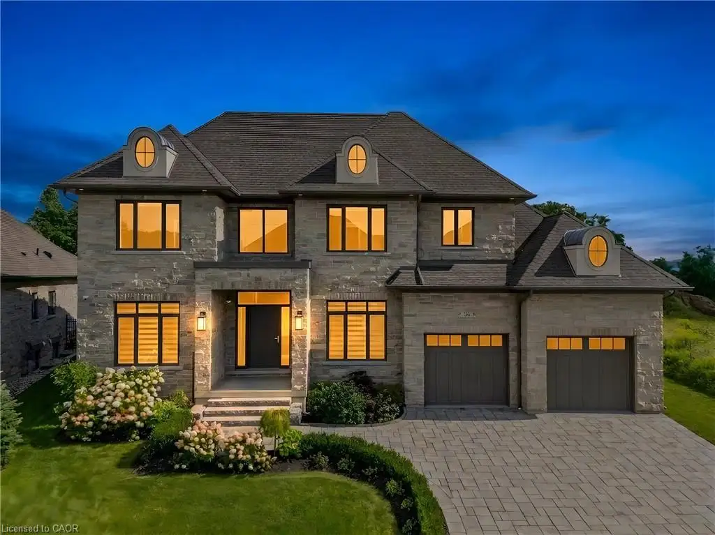 Stone-clad exterior with a prominent entry, dormer windows, a two-car garage, and a paver driveway