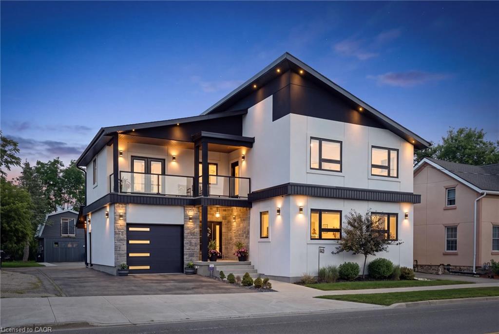 Modern architectural design featuring a glass-paneled balcony, an integrated garage, and exterior accent lighting