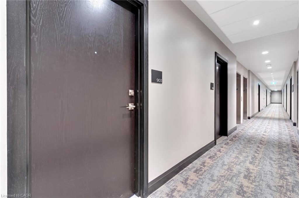 Long hallway with patterned carpeting, recessed ceiling lighting, and light-toned walls