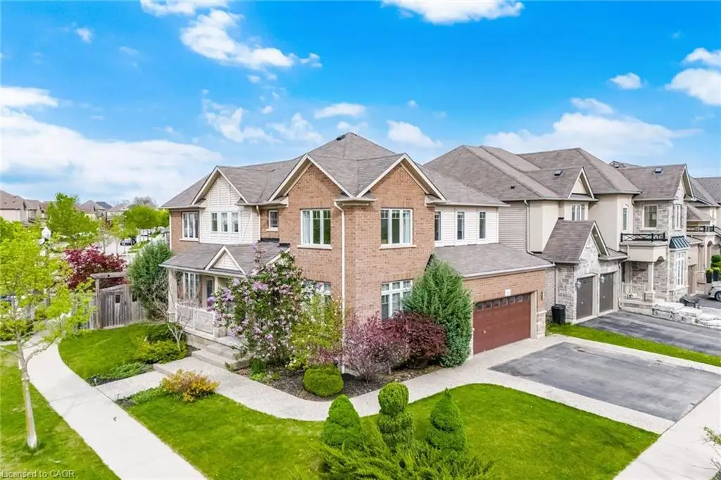 Brick and stone facade residence featuring a covered front porch, two-car garage, established landscaping, concrete driveway, and a paved walkway
