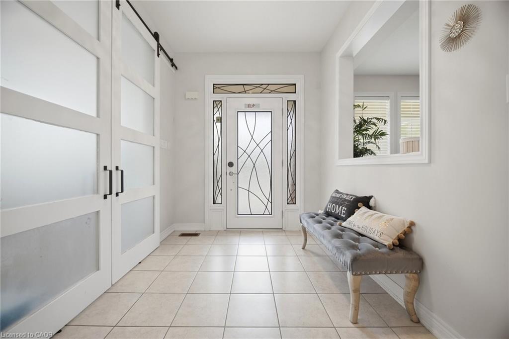 Foyer featuring tile flooring, a decorative glass entry door with sidelights, a transom window, and white barn-style sliding closet doors with frosted panels and black hardware